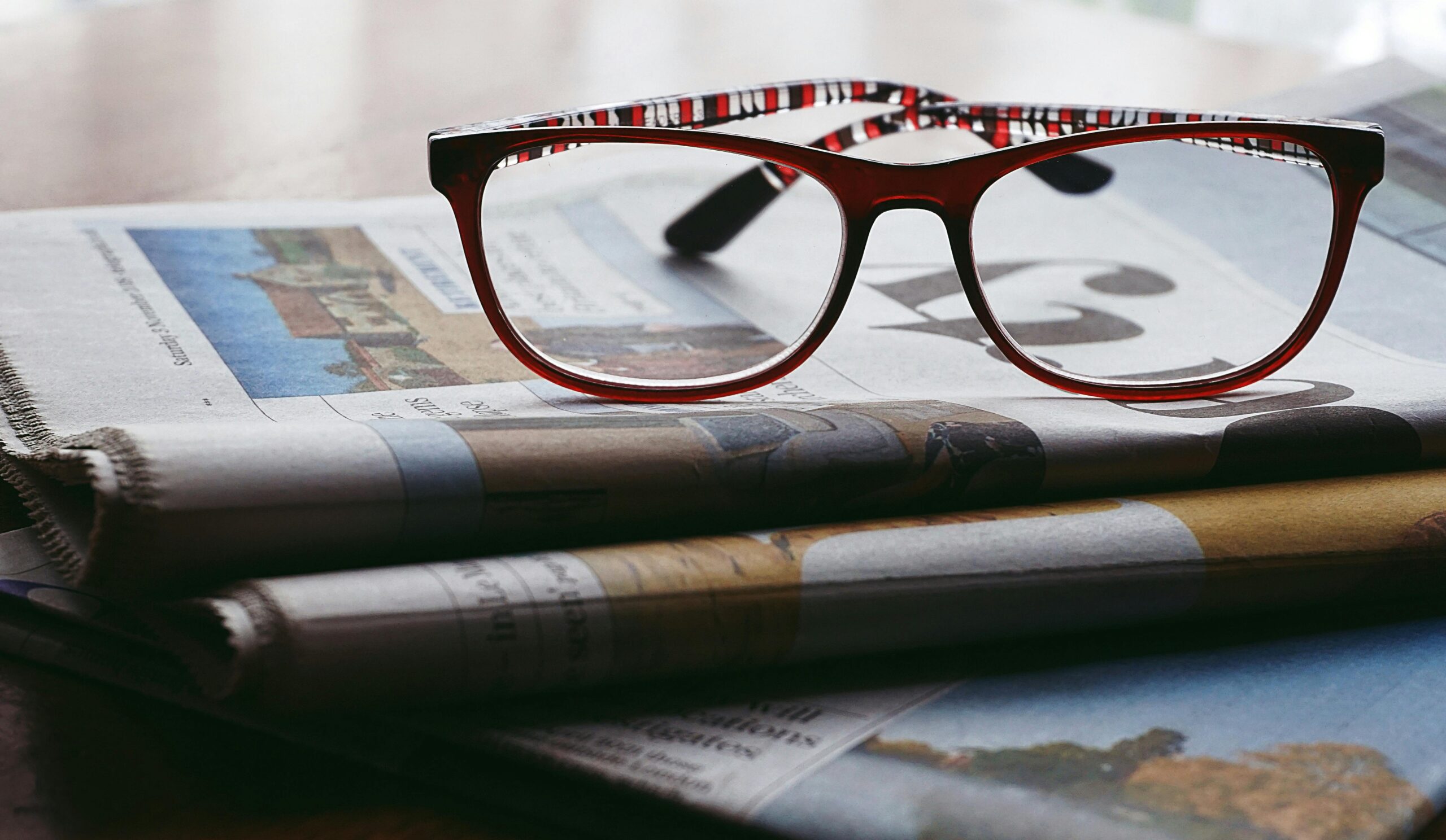 Close-up of reading glasses resting on a stack of newspapers, symbolizing knowledge and study.